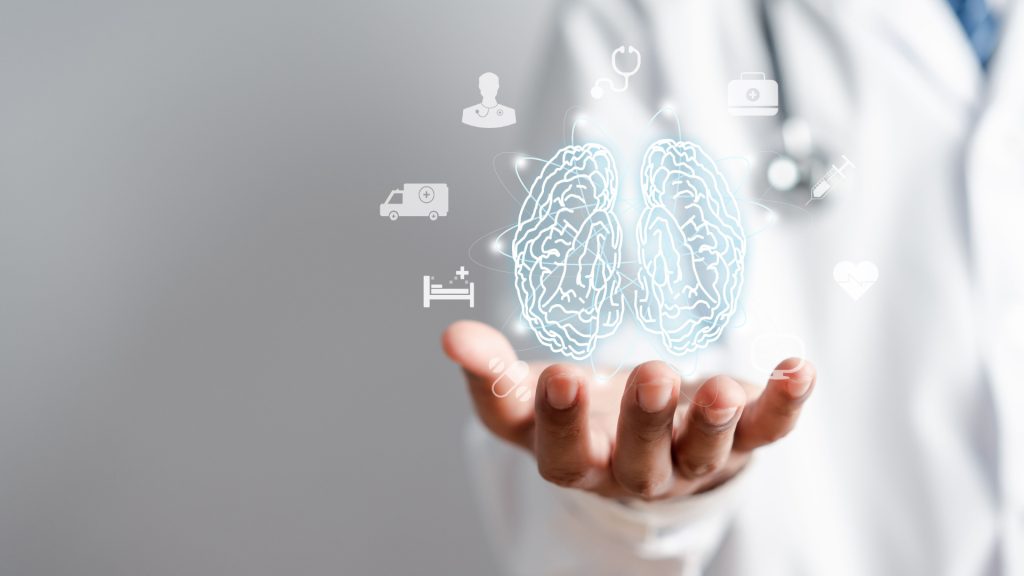 A hand is holding a brain, suggesting a symbolic representation of thought or intelligence. The setting appears to be indoors, and the focus is on the person’s hand interacting with the brain. The image conveys themes related to mental processes or cognitive functions.